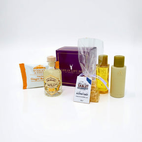 The Wee Goatfell Gift Box features a ginger soap bar, Secret Garden Organic Wild Gin mini, tablet sweets, toiletries, and a purple Isle of Arran Scottish gift box—all beautifully arranged on a white background.
